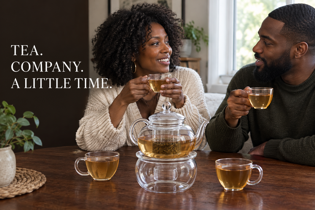 Two Black adults sharing tea at a table with a clear glass teapot, warmer, and four handled cups